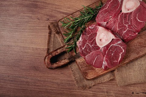 Knuckle on the bone, raw meat for ossobuco, on a wooden chopping board, with a sprig of rosemary,