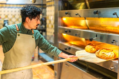 Latin young man baking bread in a traditional oven using a wooden peel