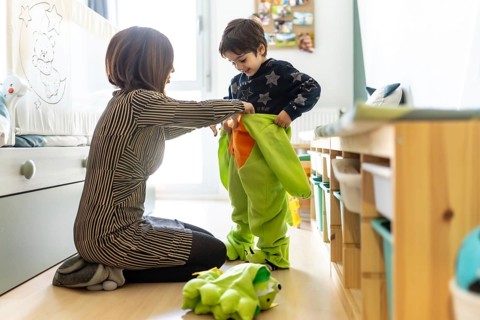 Mother assisting her son in putting on a colorful dinosaur costume, enjoying playful moments