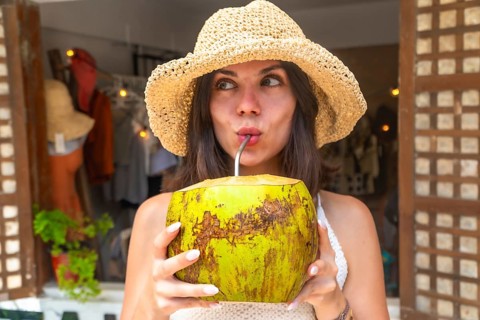 Young woman wearing straw hat enjoying refreshing coconut water during tropical vacation in siargao