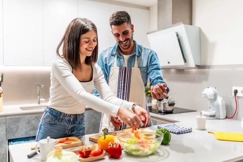 Young couple smiling and preparing a vibrant, healthy salad together in their modern kitchen,