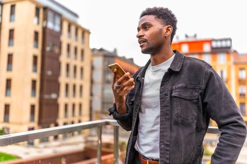 African man holding mobile sending a voice message with city views in the background