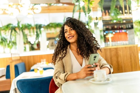 Distracted beauty latin woman using mobile while drinking coffee at cafeteria