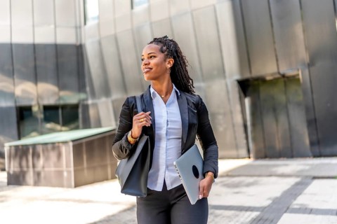 Portrait of a latin businesswoman walking distracted carrying laptop in the city next to a modern