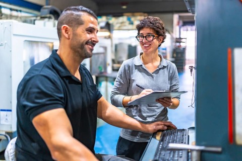 Manager and worker talking while working using computer in a cnc metal factory