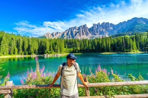 Hiker admiring the stunning turquoise waters of lake carezza with the latemar mountain range in the