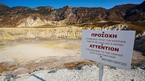 Warning sign in front of volcanic crater in sunny mountainous landscape, volcanism, volcanic