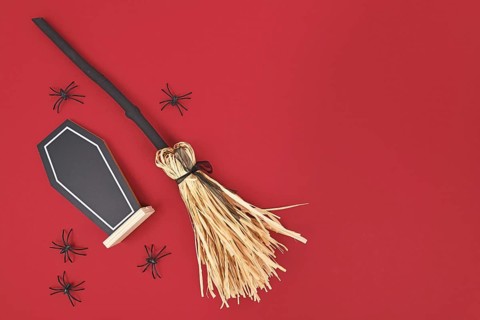 Halloween witch broom, coffin shaped chalkboard and spiders on dark red background with copy space