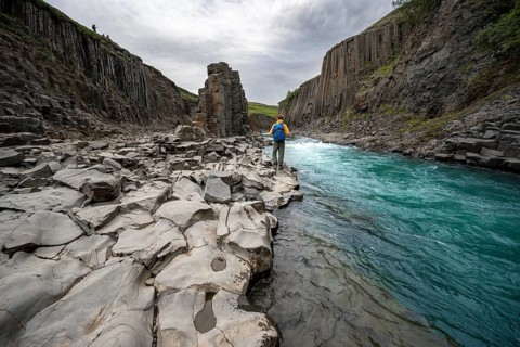Tourist standing by the river in Stuðlagil Canyon, turquoise blue river between basalt columns,