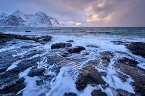 Beach of Norwegian sea on rocky coast in fjord on sunset in winter. Vareid beach, Lofoten islands,