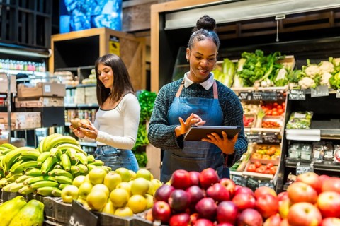 Friendly saleswoman using digital tablet and managing organic products while customer choosing
