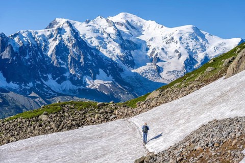 Mountaineer crossing a snowfield, view of spectacular glaciated peaks of Mont Blanc, Mont Blanc