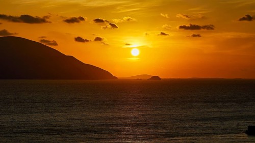 Sunset over the sea with sunbeams and an island on the horizon, warm yellow tones dominate, sunset,