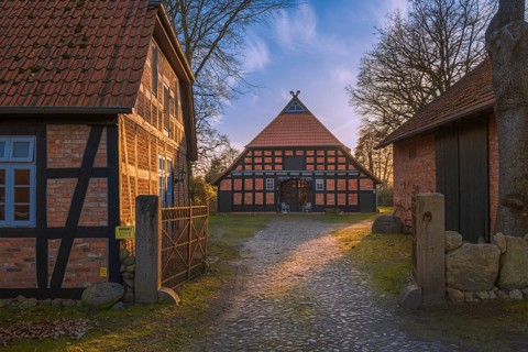 View of a courtyard entrance with a half-timbered farmhouse behind it in the evening light,