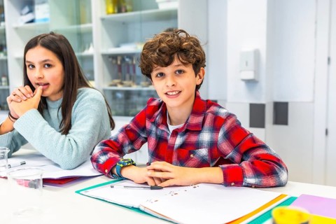 Smiling students sitting at desk in science classroom, learning and interacting during lesson,