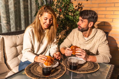 Happy couple enjoying burgers and wine on a cozy terrace, creating a romantic and intimate