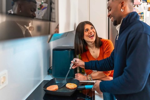 Cheerful multiethnic couple laughing and having fun while preparing burgers together on the