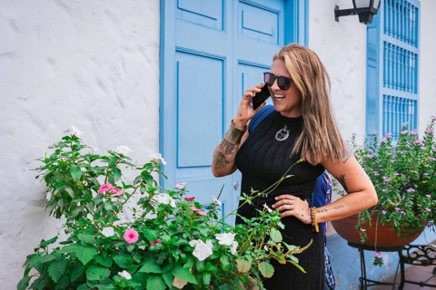 A joyful middle-aged woman with straight hair and a curvy Latin figure chats on the phone in front