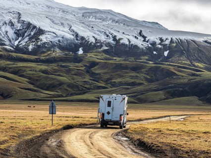 Pickup camper on gravel road, early snow on mountain range, along road Landmannaleid F225,