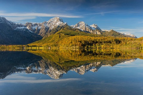Lake Almsee in autumn with mountains reflected in the lake. Blue sky