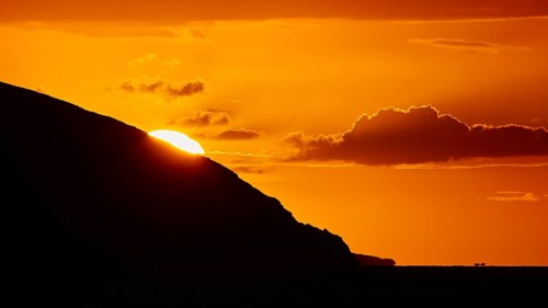 Soft orange light of the sun behind a mountain, cloud formations in the sky, sunset, Kassos,