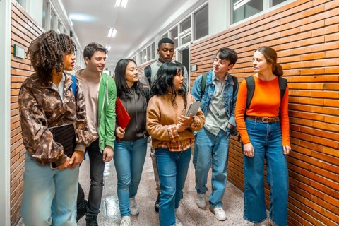 Group of diverse university students walking down school hallway, discussing and collaborating on