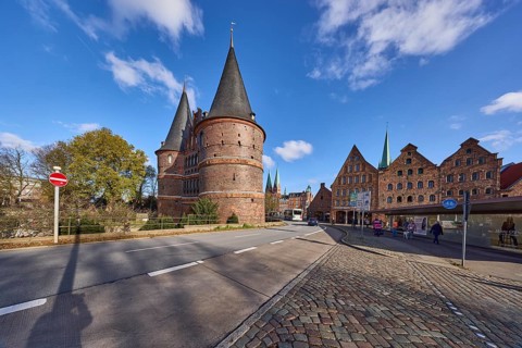 Lübeck Holstentor, side view, pedestrian crossing, cobblestone pavement, blue sky with fair weather