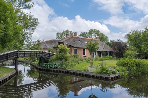 Large house with water reflection and wooden bridge in a peaceful, natural setting, Giethoorn,