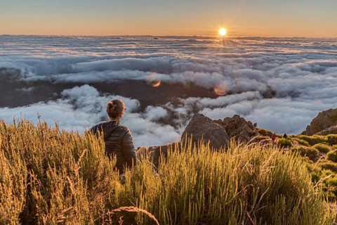 A hiker watches the sunset over a sea of clouds from a mountain top, Pico Ruivo, Madeira, Portugal,