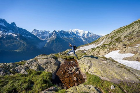 Mountaineer jumping, mountain panorama, view of mountain peaks Grandes Jorasses and Mont Blanc,