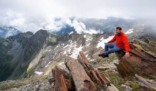 Mountaineer sitting on a rock, cloudy mountain landscape at the summit of Lasörling, view to Berger