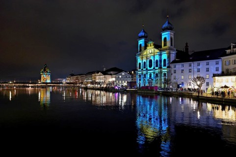 Water tower and Jesuit church on the right with light installation, on the Reuss at dusk, Old Town,