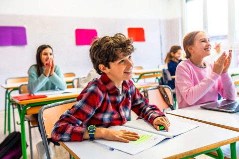 Elementary school students sitting at desks, attentively listening to the teacher while taking