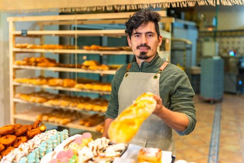 Latin young friendly baker offering freshly baked baguette in an artisan bakery shop