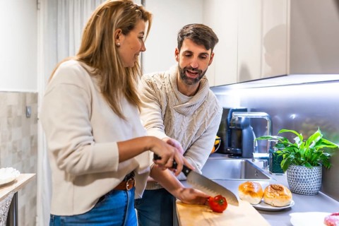 Young couple preparing a burger for dinner, slicing fresh tomatoes on a wooden cutting board in