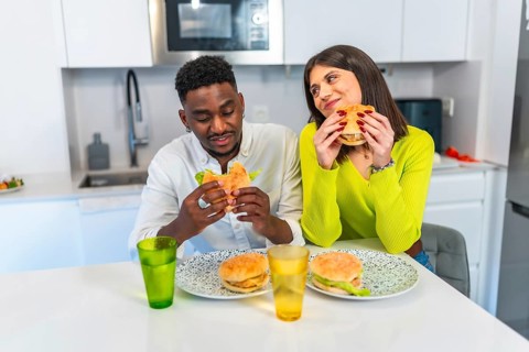 Young multiethnic couple savoring delicious burgers together in their contemporary kitchen,