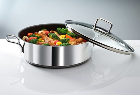 Cooking pot with vegetables and chicken thighs in front of a white background, studio shot