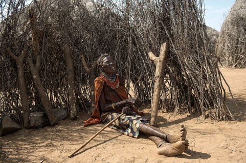 Old woman sitting in front of a fence made of wooden sticks and small tree trunks, Karo ethnic