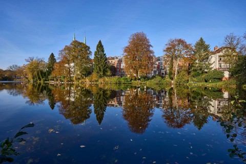 Mill pond with trees, general buildings against a cloudless blue sky, symmetrical reflections on