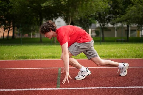 Side view full length of a caucasian young male runner in the starting line of a track ready to