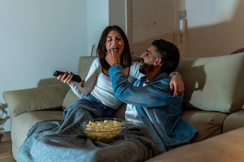 Young couple relaxing on the sofa, enjoying popcorn and watching television together during a cozy