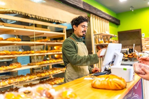 Salesman using touchscreen computer to calculate the bill of a client in the counter of bakery shop