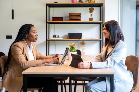 Two businesswomen are working together on a project using a laptop and tablet in a hotel lobby