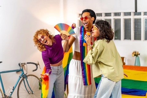 Multi-ethnic friends celebrating pride with rainbow hand fan and flags having fun at home