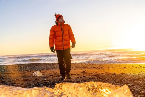 A tourist in an orange jacket walking at sunrise on Diamond Beach Iceland in winter