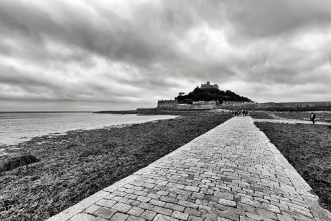Walker, cobbled causeway, St Michael's Mount, tidal island with castle, dramatic cloudy sky,