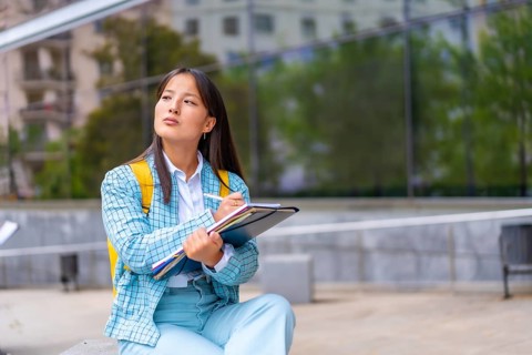 Portrait three quarter length of a beauty Asian student writing notes sitting on the campus looking