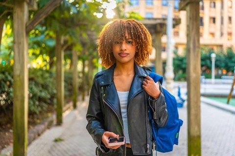 Frontal portrait of a beauty and confident latin woman using smartphone walking down the street