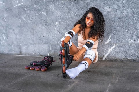 Latin beauty woman putting on inline skates, sitting in front of an urban wall, wearing pink