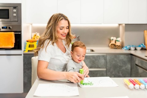 Smiling mother and son enjoying a fun painting session with dot markers, sitting together at the